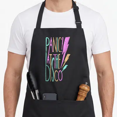 Panic disco apron - Stacked text PANIC! AT THE DISCO with three teal pink and orange lightning bolts — shown on a black cotton canvas apron against a white background