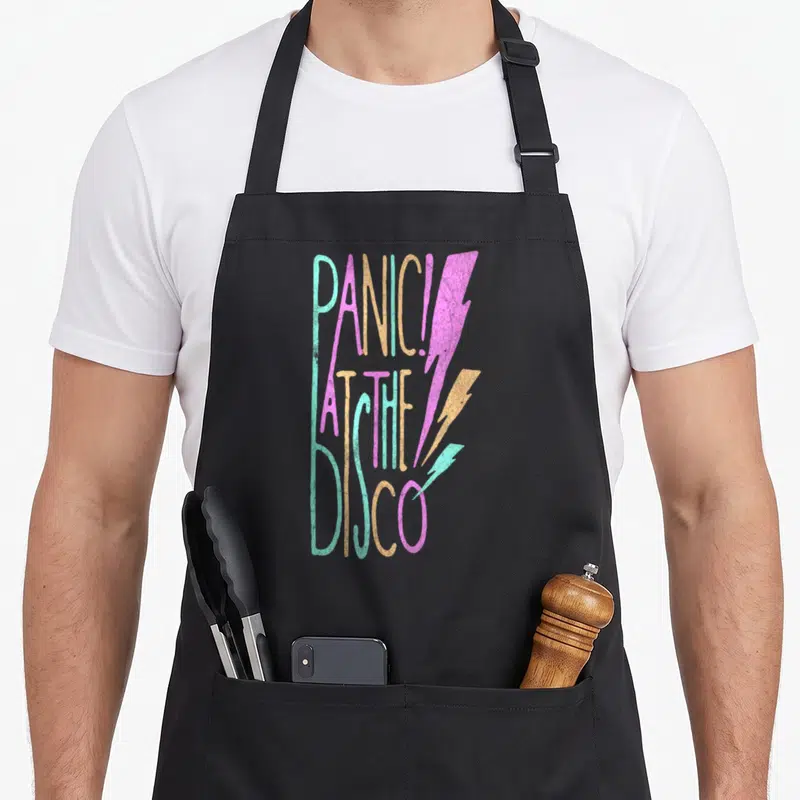 Panic disco apron - Stacked text PANIC! AT THE DISCO with three teal pink and orange lightning bolts — shown on a black cotton canvas apron against a white background
