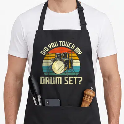 Drummer touch drum apron - Retro drum set graphic with Did You Touch My text over striped sunset background — shown on a black cotton canvas apron against a white background
