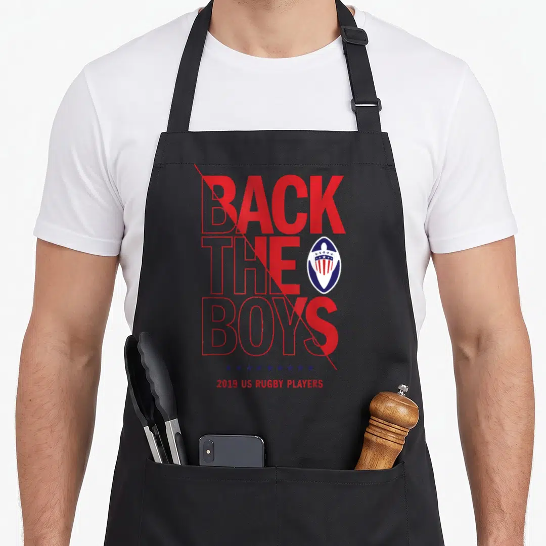 Rugby police squad apron - Red and blue Back the Boys 2019 US Rugby Players text with stars and logo on black fabric — shown on a black cotton canvas apron against a white background