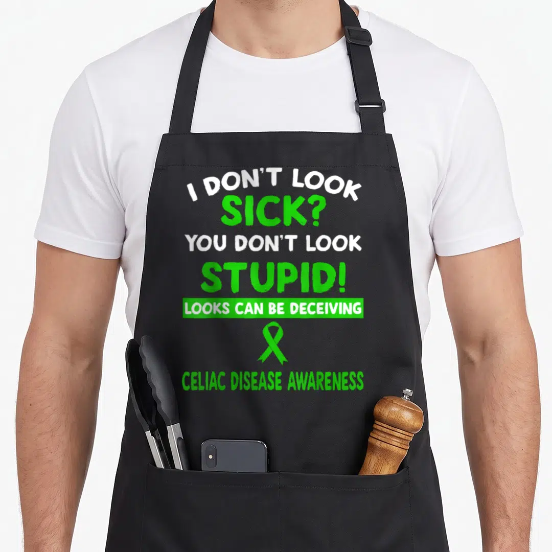 Deceiving celiac awareness apron - Green and white typography with awareness ribbon and sarcasm about invisible illness — shown on a black cotton canvas apron against a white background