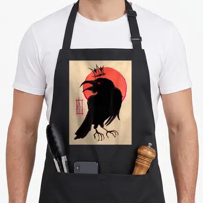 Corvid king apron - Black crow standing before red circle with floating crown and abstract symbol on beige background — shown on a black cotton canvas apron against a white background