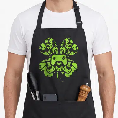 Video game st patrick day aprons - Lime green shamrock shape formed by cluster of video game controller silhouettes — shown on a black cotton canvas apron against a white background