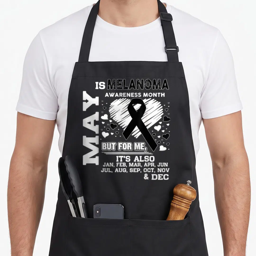 May melanoma awareness apron - Black ribbon over white heart with distressed text listing all twelve months of the year — shown on a black cotton canvas apron against a white background