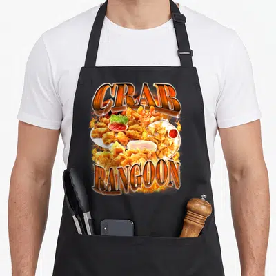 Meme crab apron - Arched CRAB RANGOON text framing fried dumplings, red sauce, and lettuce surrounded by orange flames — shown on a black cotton canvas apron against a white background