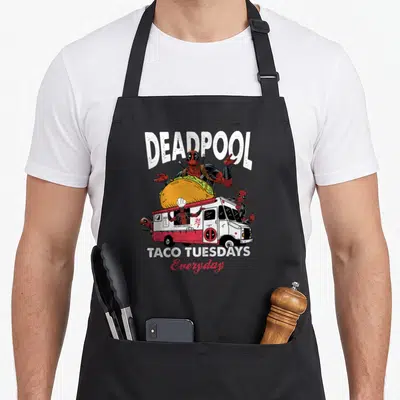 Tuesday taco apron - Deadpool holding giant taco on food truck with TACO TUESDAYS Everyday text — shown on a black cotton canvas apron against a white background
