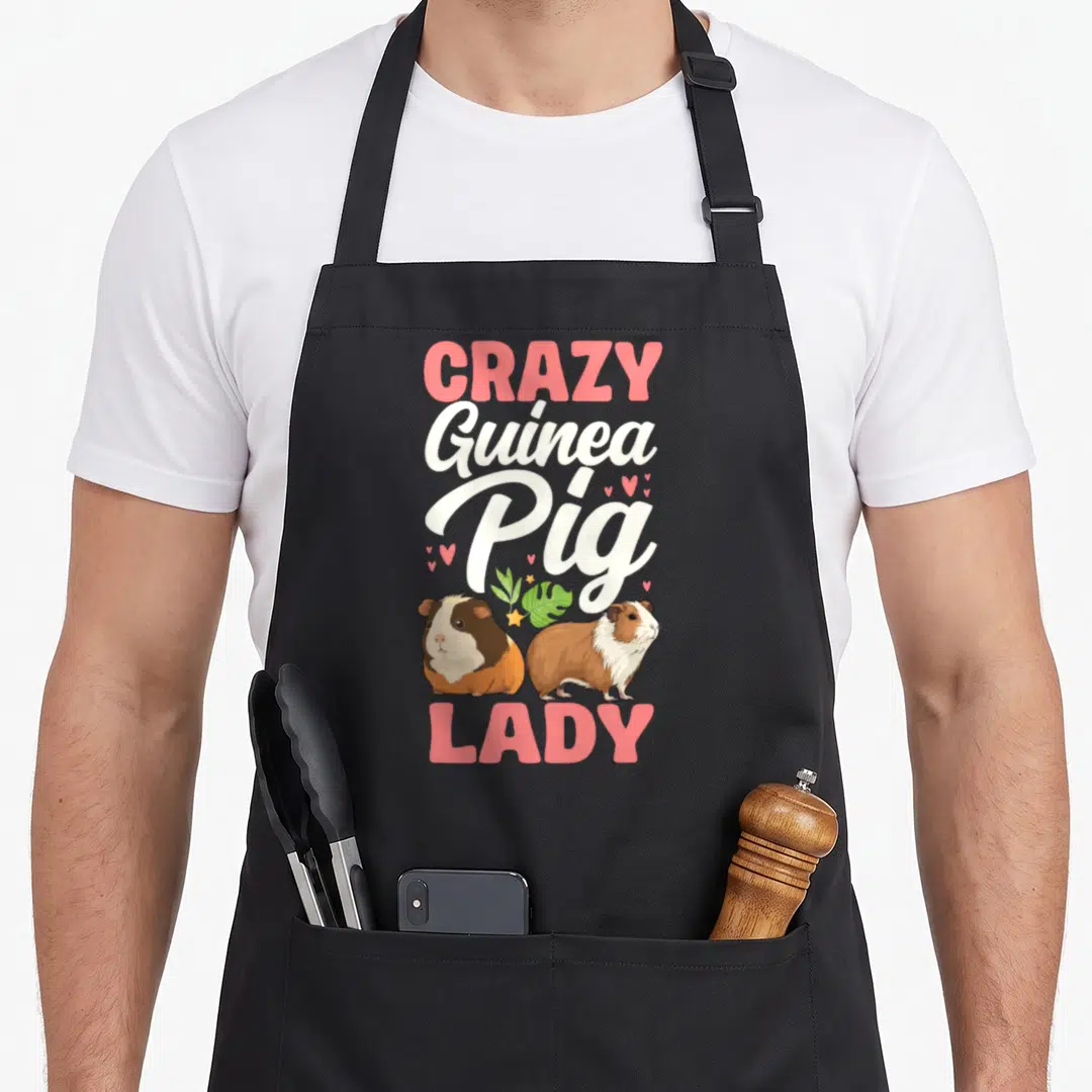 Creature crazy guinea lady apron - Stacked text reading CRAZY Guinea Pig LADY above two cartoon guinea pigs with hearts — shown on a black cotton canvas apron against a white background