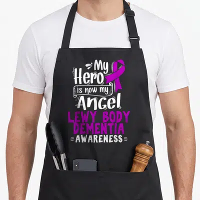 Lewy body apron - Purple ribbon and white text reading My Hero is now my Angel Lewy Body Dementia Awareness — shown on a black cotton canvas apron against a white background