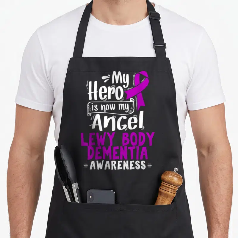 Lewy body apron - Purple ribbon and white text reading My Hero is now my Angel Lewy Body Dementia Awareness — shown on a black cotton canvas apron against a white background