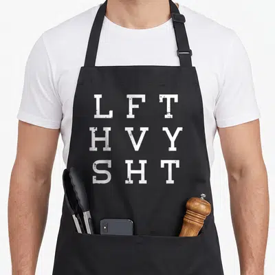Gym heavy apron - White LFT HVY SHT block letters stacked vertically on a black background — shown on a black cotton canvas apron against a white background