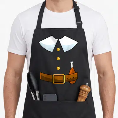 Collar pilgrim apron - Cartoon grey outfit with white collar, three yellow buttons, brown belt, and tucked turkey leg — shown on a black cotton canvas apron against a white background