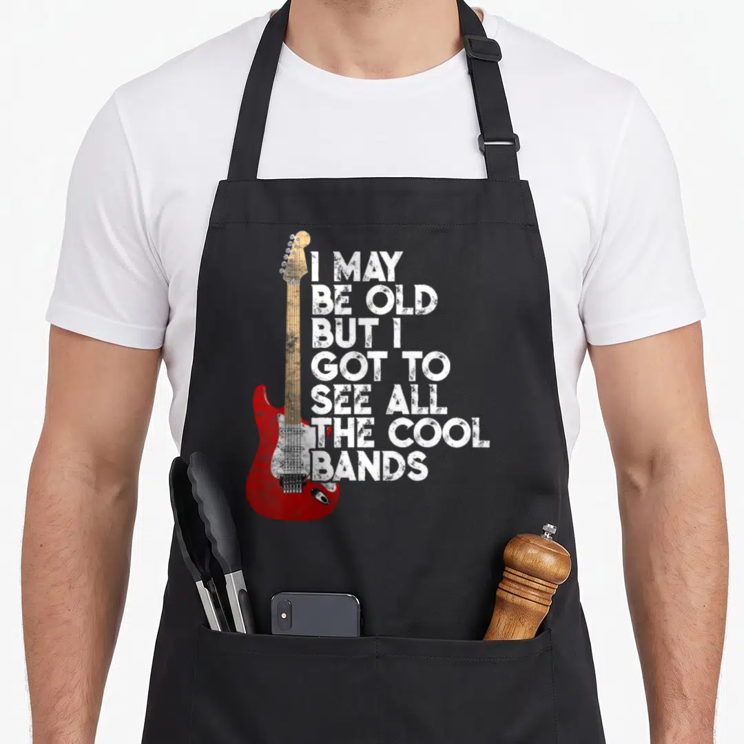 See but cooler apron - Red electric guitar with tan neck beside seven lines of distressed white text reading I MAY BE — shown on a black cotton canvas apron against a white background