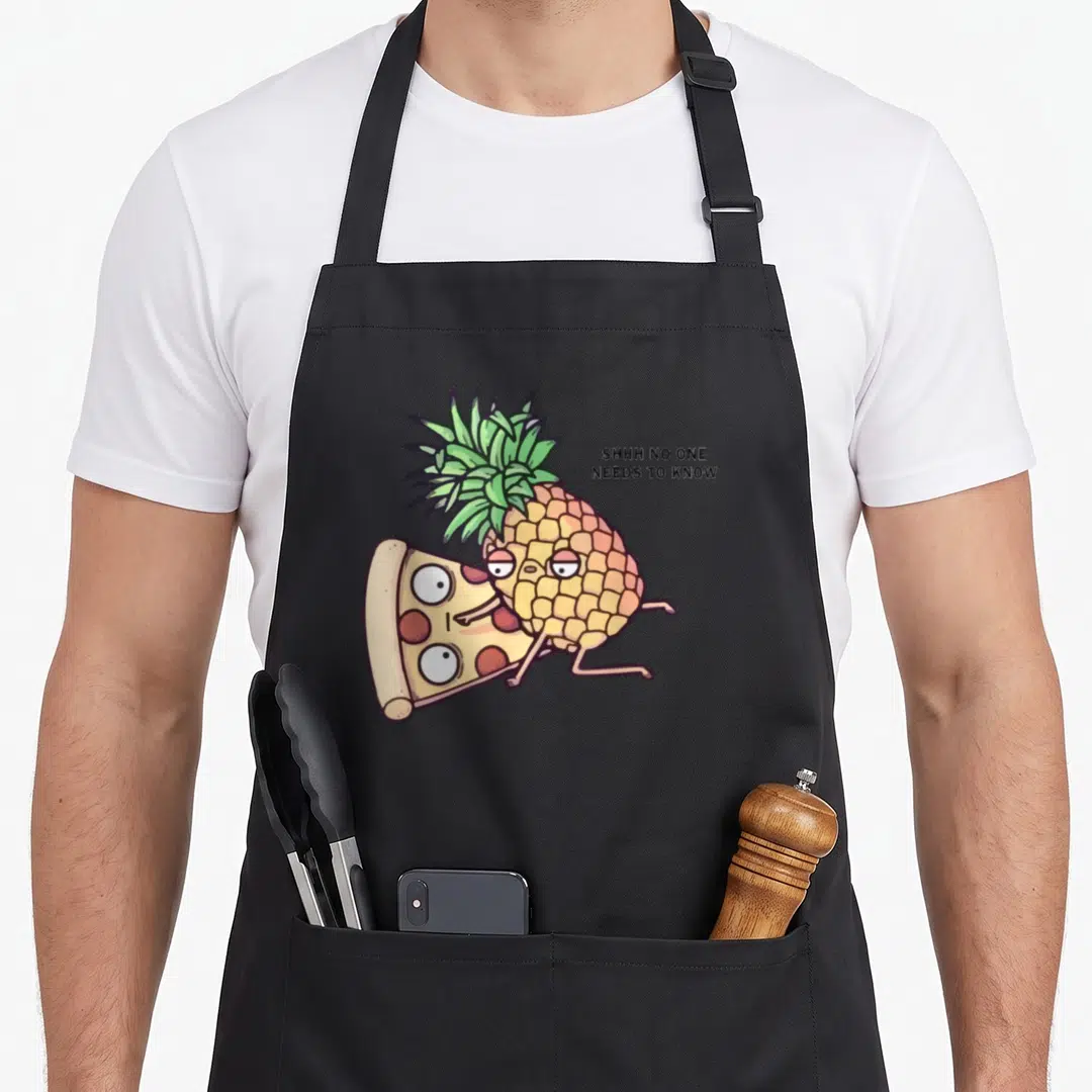 Belong pineapple apron - Cartoon pineapple hugging pizza slice with text SHHH NO ONE NEEDS TO KNOW — shown on a black cotton canvas apron against a white background