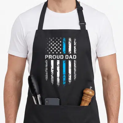 Law patriotic apron - PROUD DAD text over distressed flag with vertical white and blue stripes — shown on a black cotton canvas apron against a white background
