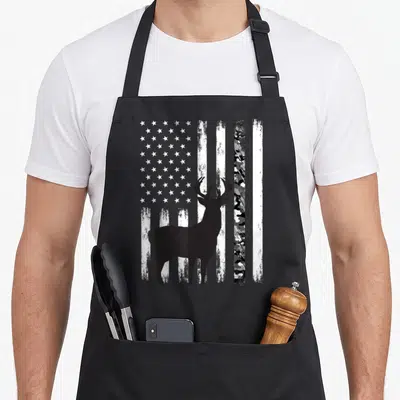 Hunting camo aprons - Black deer silhouette over distressed monochrome flag with camo stripe — shown on a black cotton canvas apron against a white background