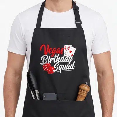 Las vegas birthday apron - Red and white Vegas Birthday Squad text with playing cards and dice on black — shown on a black cotton canvas apron against a white background