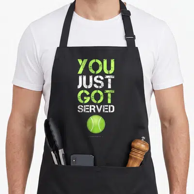 Served tennis hobby apron - Stacked YOU JUST GOT SERVED text above lime green tennis ball with distressed font — shown on a black cotton canvas apron against a white background