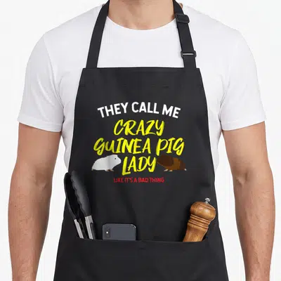 They crazy guinea lady apron - Stacked text they call me crazy guinea pig lady like its a bad thing with two rodent — shown on a black cotton canvas apron against a white background