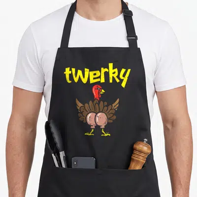 Twerky thanksgiving apron - Yellow twerky text above a cartoon turkey seen from behind with brown feathers and a red — shown on a black cotton canvas apron against a white background