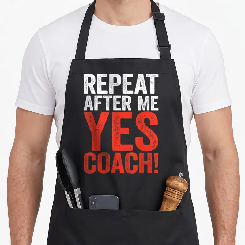 Repeat coaching apron - Stacked distressed text reading REPEAT AFTER ME YES COACH in white and red block letters — shown on a black cotton canvas apron against a white background