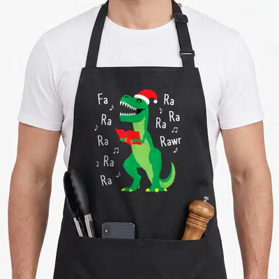 Rawr santa apron - Green dinosaur in red Santa hat holding red book with Fa Ra Ra Rawr text — shown on a black cotton canvas apron against a white background