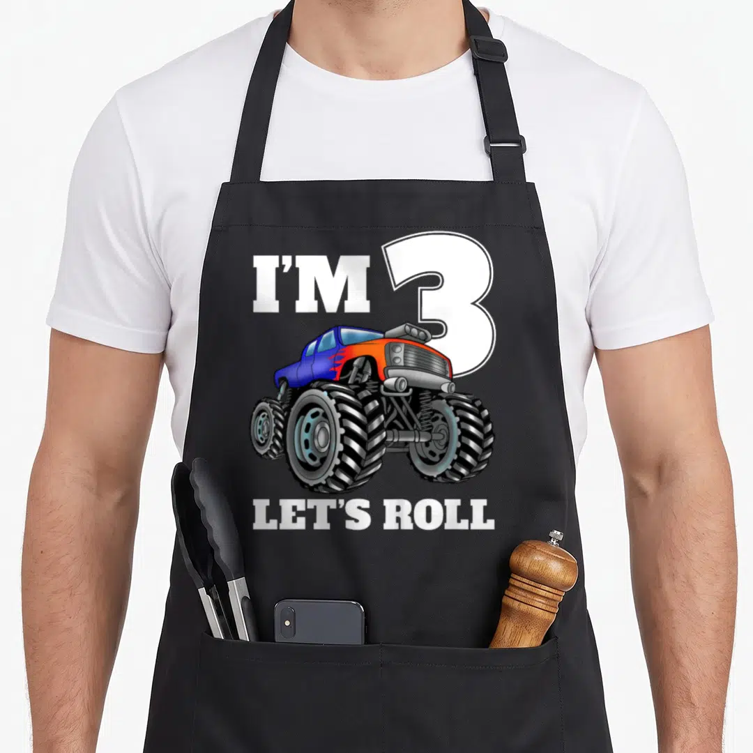 Birthday three truck apron - Cartoon monster truck in blue and orange overlapping large white number 3 with text I'M 3 — shown on a black cotton canvas apron against a white background