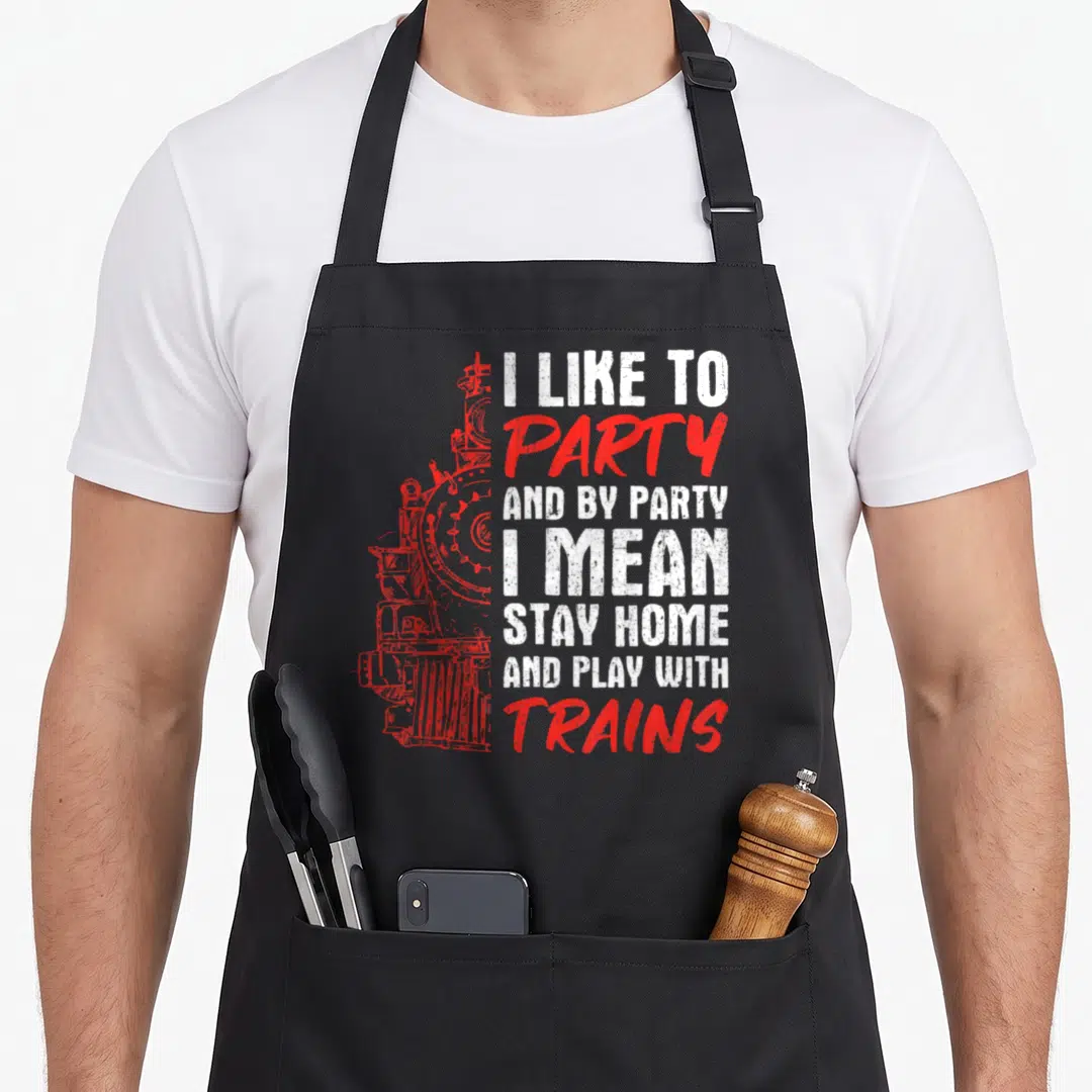 Model stay home apron - Red distressed train graphic next to white and red text about staying home and playing — shown on a black cotton canvas apron against a white background