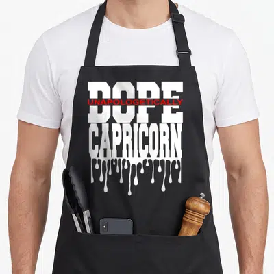 Dope queen king apron - Stacked white and red text reading DOPE UNAPOLOGETICALLY CAPRICORN with dripping paint effect — shown on a black cotton canvas apron against a white background