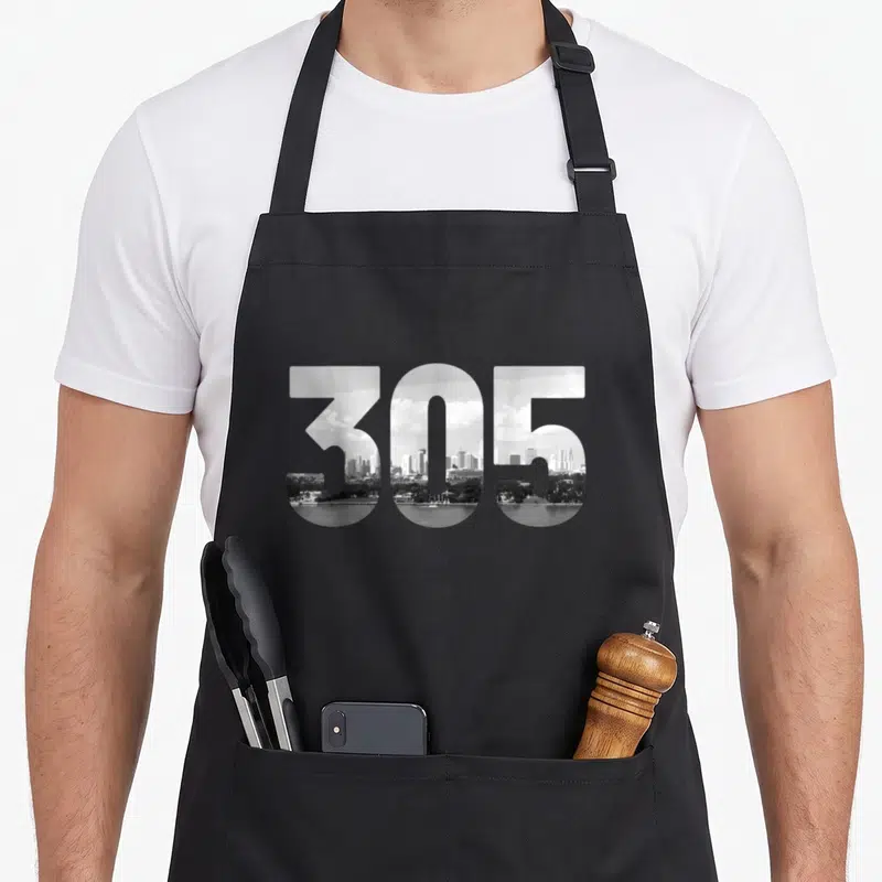 Code florida apron - 305 area code filled with grayscale city skyline reflecting in water — shown on a black cotton canvas apron against a white background