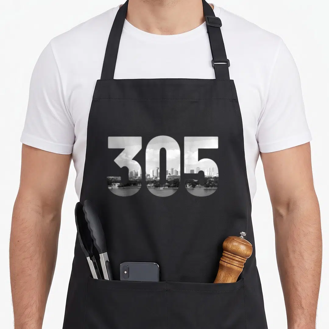 Code florida apron - 305 area code filled with grayscale city skyline reflecting in water — shown on a black cotton canvas apron against a white background