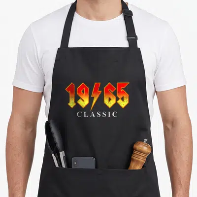 Rock 60th birthday apron - 1965 number with lightning bolt and CLASSIC text in yellow red white retro style — shown on a black cotton canvas apron against a white background