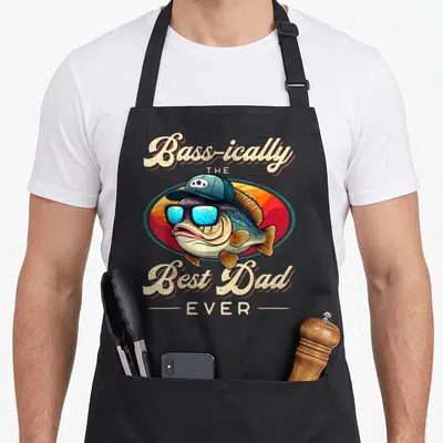 Fishing fisherman father day apron - Cartoon bass in teal cap and blue sunglasses with cream text 'Bass-ically THE Best — shown on a black cotton canvas apron against a white background