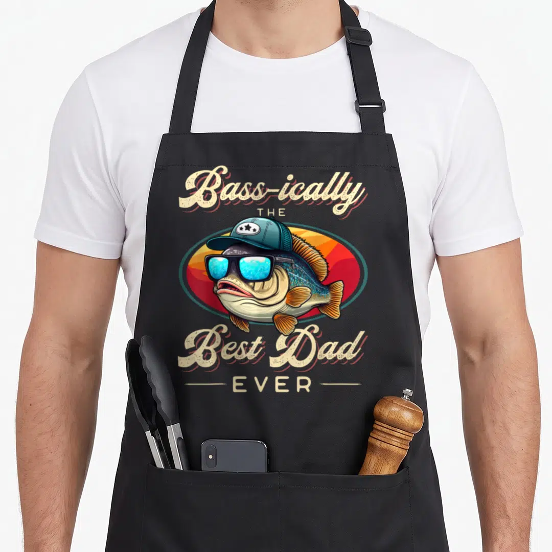 Fishing fisherman father day apron - Cartoon bass in teal cap and blue sunglasses with cream text 'Bass-ically THE Best — shown on a black cotton canvas apron against a white background
