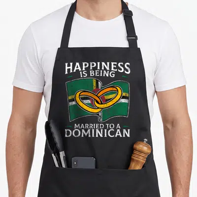 Dominica heritage aprons - Distressed text above waving flag with two interlocking gold rings — shown on a black cotton canvas apron against a white background