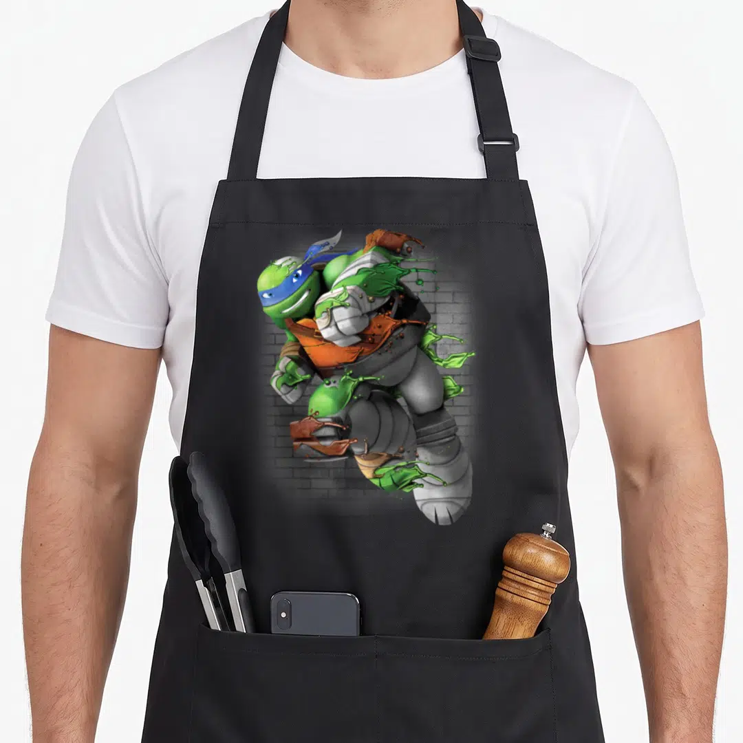 Leonardo immature apron - Realistic ninja turtle with green slime splash against grey brick wall — shown on a black cotton canvas apron against a white background