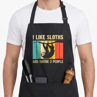 Retro sloth apron - I like sloths and maybe 3 people text with hanging sloth silhouette on teal, beige, yellow, red — shown on a black cotton canvas apron against a white background