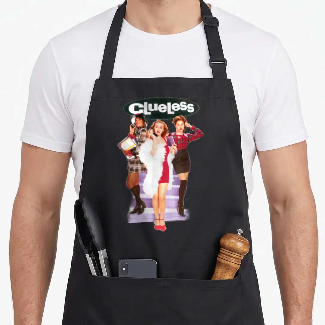 Clueless tai apron - Three women on purple stairs below white Clueless text in dark green oval — shown on a black cotton canvas apron against a white background
