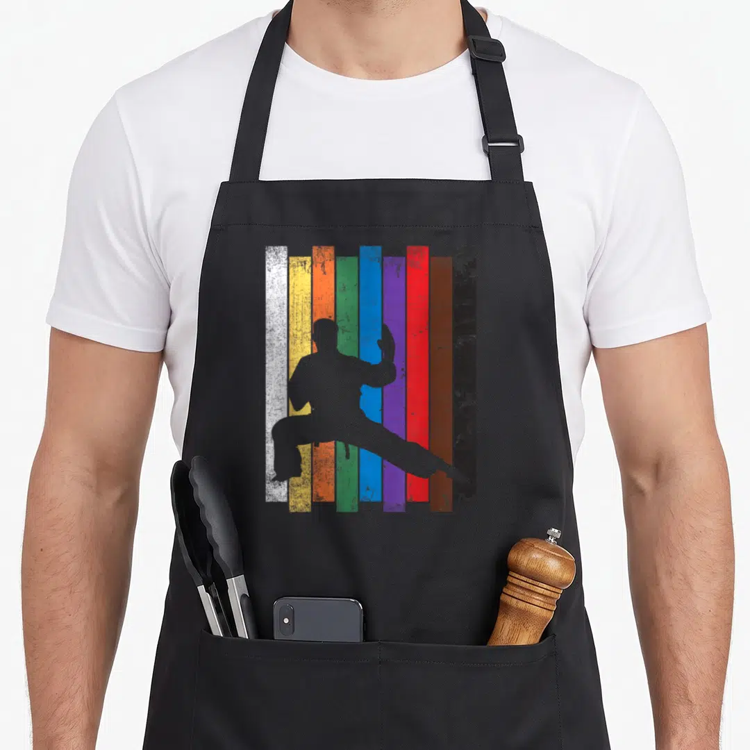 Rank karate apron - Grey martial artist silhouette over nine vertical colored stripes white to black — shown on a black cotton canvas apron against a white background