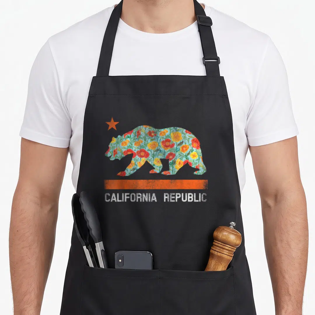 State bear apron - Floral bear silhouette with orange star, stripe, and CALIFORNIA REPUBLIC text — shown on a black cotton canvas apron against a white background