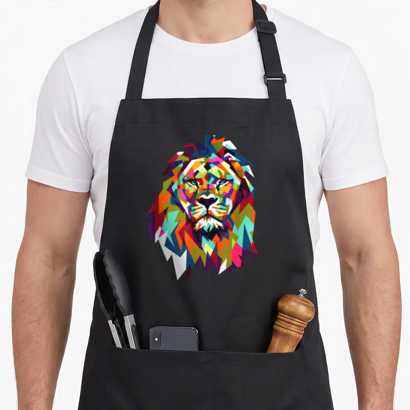 Lion face apron - Colorful geometric lion head in blue red yellow green and purple cartoon style — shown on a black cotton canvas apron against a white background