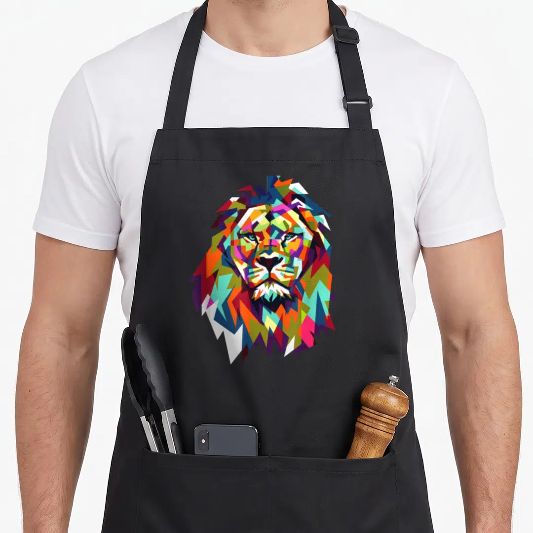 Lion face apron - Colorful geometric lion head in blue red yellow green and purple cartoon style — shown on a black cotton canvas apron against a white background