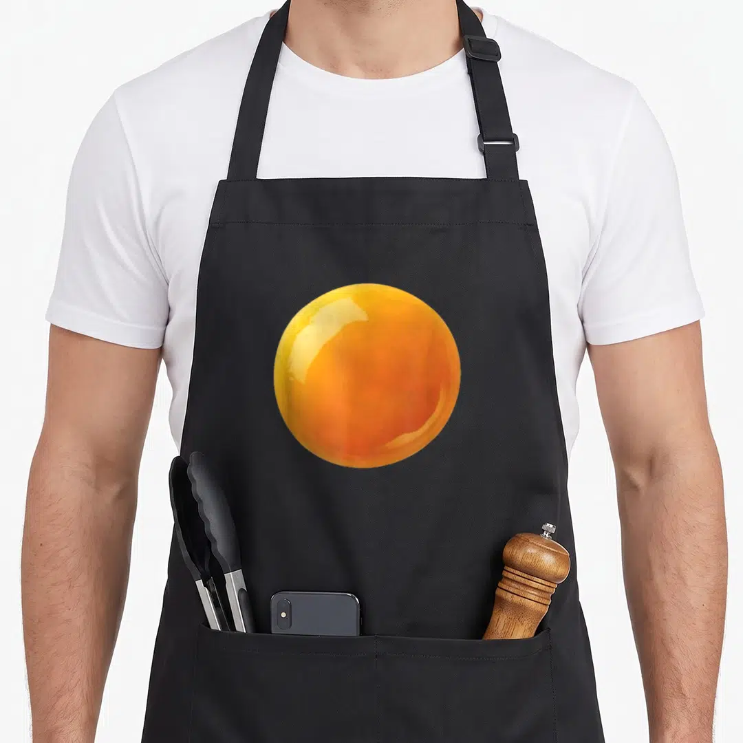 Couple egg apron - Realistic orange and yellow sphere resembling a deviled egg yolk on fabric — shown on a black cotton canvas apron against a white background