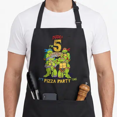 Dude pizza apron - Four turtles holding pizza around number 5 and text DUDE! I'M 5 IT'S PIZZA PARTY TIME — shown on a black cotton canvas apron against a white background