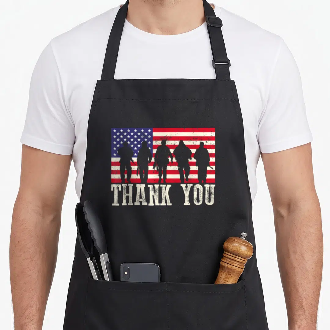 Thank american flag apron - Five grey soldier silhouettes over distressed red white and blue flag with THANK YOU text — shown on a black cotton canvas apron against a white background