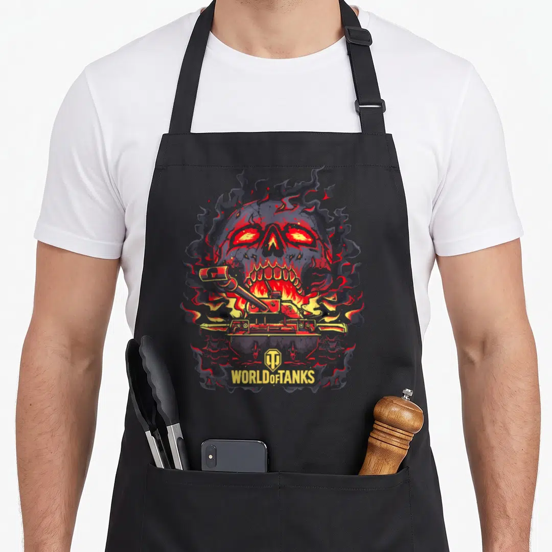 Fire skull halloween apron - Flaming grey skull with red eyes, yellow tank in mouth, and WORLD OF TANKS text at bottom — shown on a black cotton canvas apron against a white background