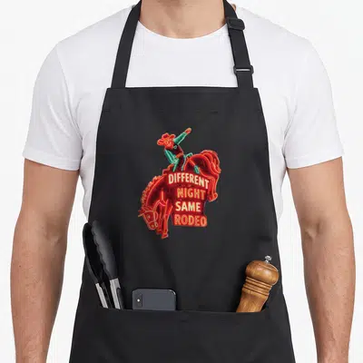 Different baileys apron - Neon cowboy riding horse with DIFFERENT NIGHT SAME RODEO text stacked on red body — shown on a black cotton canvas apron against a white background