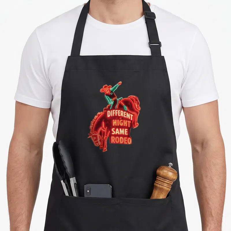 Different baileys apron - Neon cowboy riding horse with DIFFERENT NIGHT SAME RODEO text stacked on red body — shown on a black cotton canvas apron against a white background