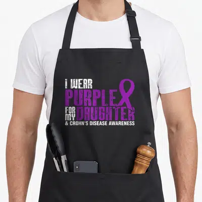 Daughter crohns awareness apron - Purple and white stacked text reading I WEAR PURPLE FOR MY DAUGHTER with a ribbon — shown on a black cotton canvas apron against a white background