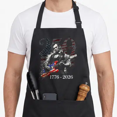 250th day july apron - Abraham Lincoln playing flag-patterned guitar with 250 Years text and 1776-2026 dates on grey — shown on a black cotton canvas apron against a white background