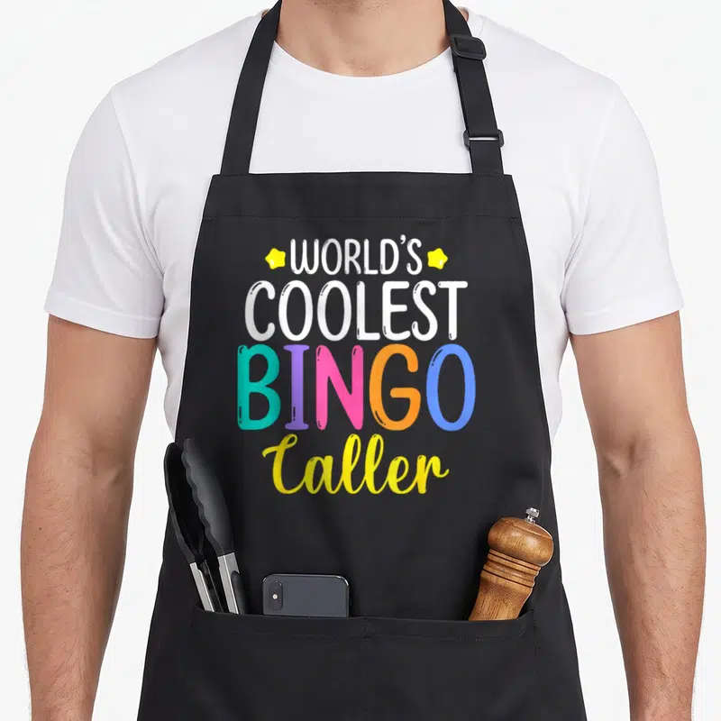 Player coolest bingo aprons - Stacked text reading World's Coolest Bingo Caller with multi-colored letters and yellow — shown on a black cotton canvas apron against a white background